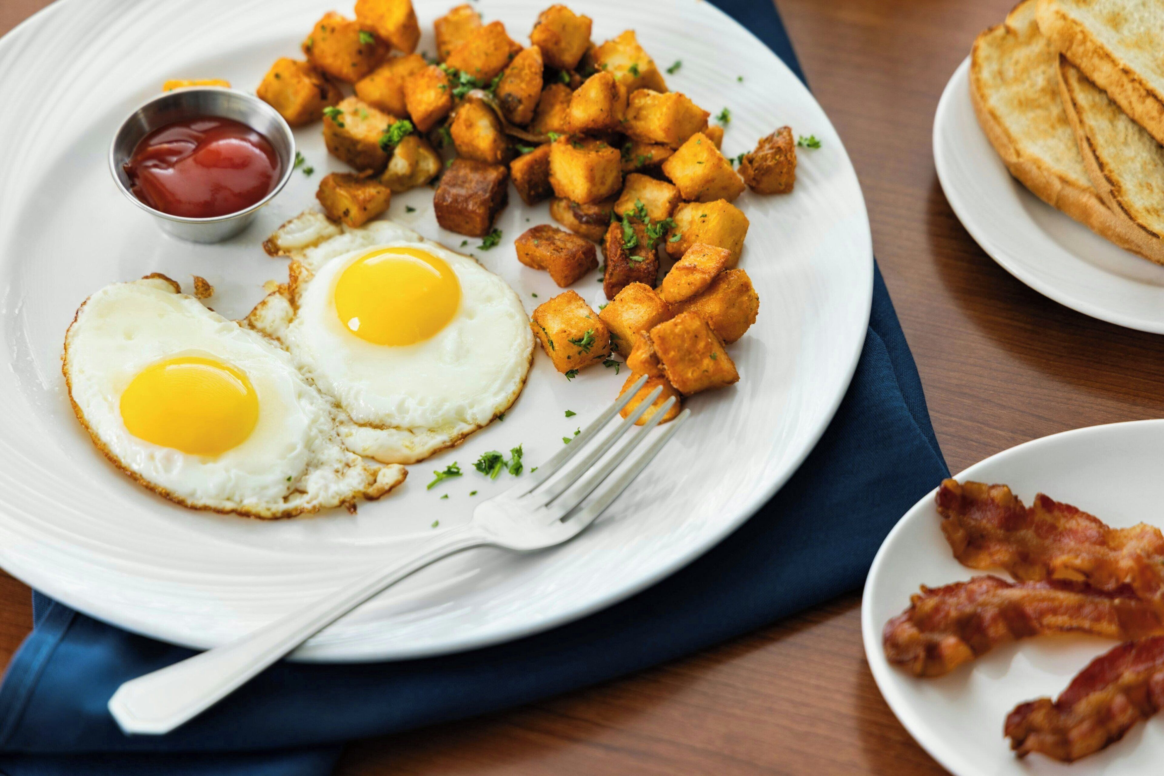 Ein Teller mit gebratenen Eiern, Kartoffelrösti und Speck.