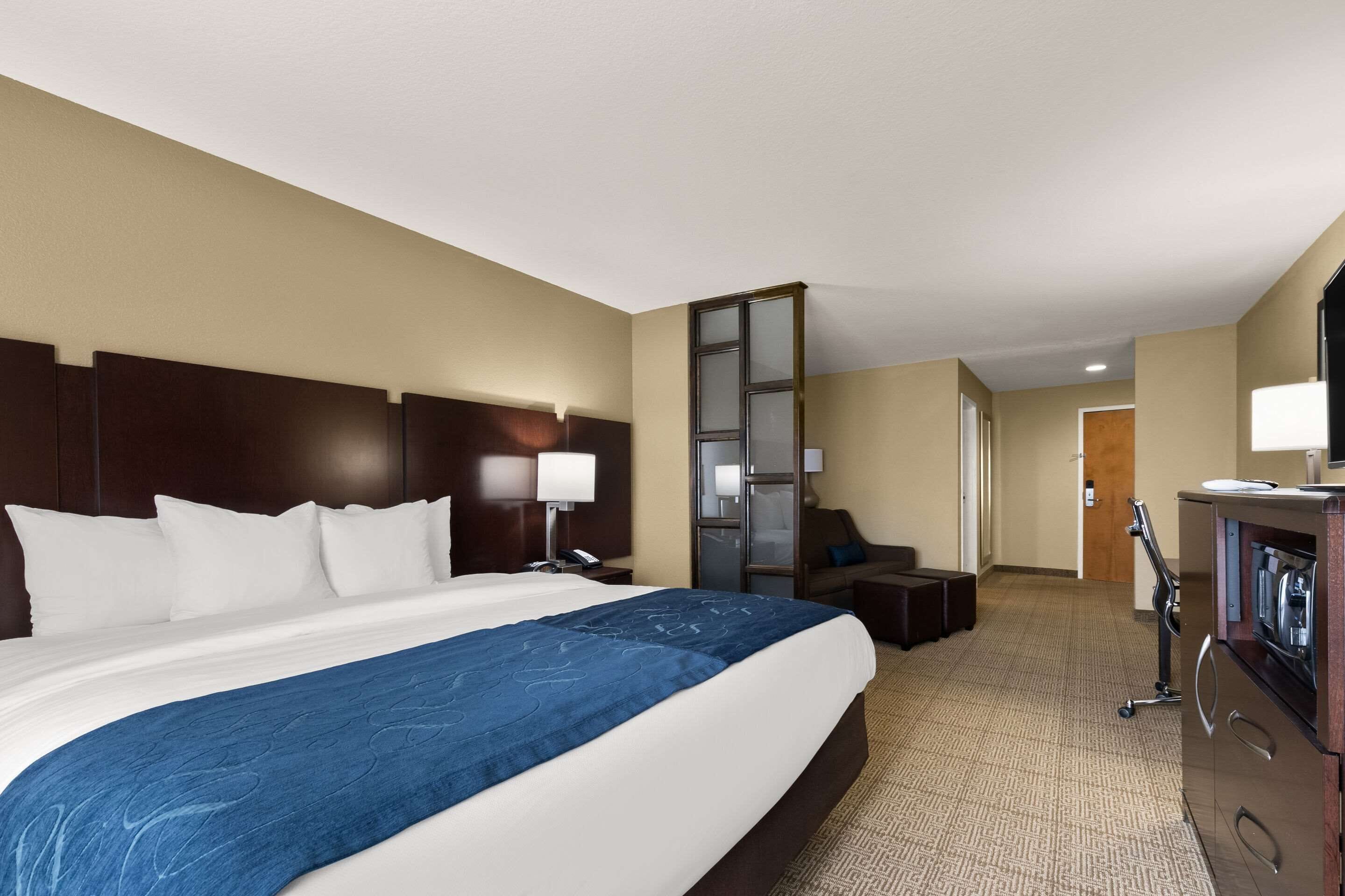 Quarto de hotel com uma cama grande, uma escrivaninha, uma cadeira, uma TV e um minibar.