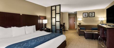 A hotel room with a large bed, a desk, a chair, a TV, and a sofa.
