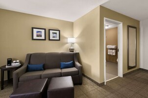 Una habitación de hotel con un sofá, una mesita con una lámpara y una puerta que da a un baño.
