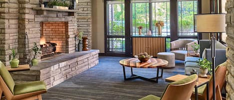 A spacious living area with a stone fireplace, comfortable seating, and large windows offering a view of greenery.