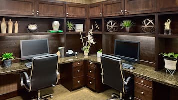 A modern office with two desks, each with a computer and chair, surrounded by dark wood cabinets and shelves with decorative items.