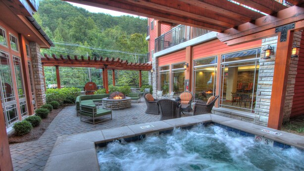 A hot tub area with seating and a fire pit, surrounded by a patio with a view of a forested hillside.