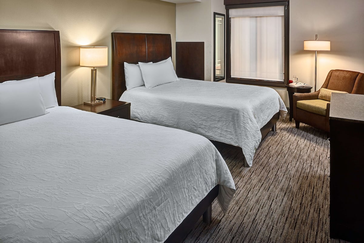 A hotel room with two beds, a chair, a desk, and a window with curtains.