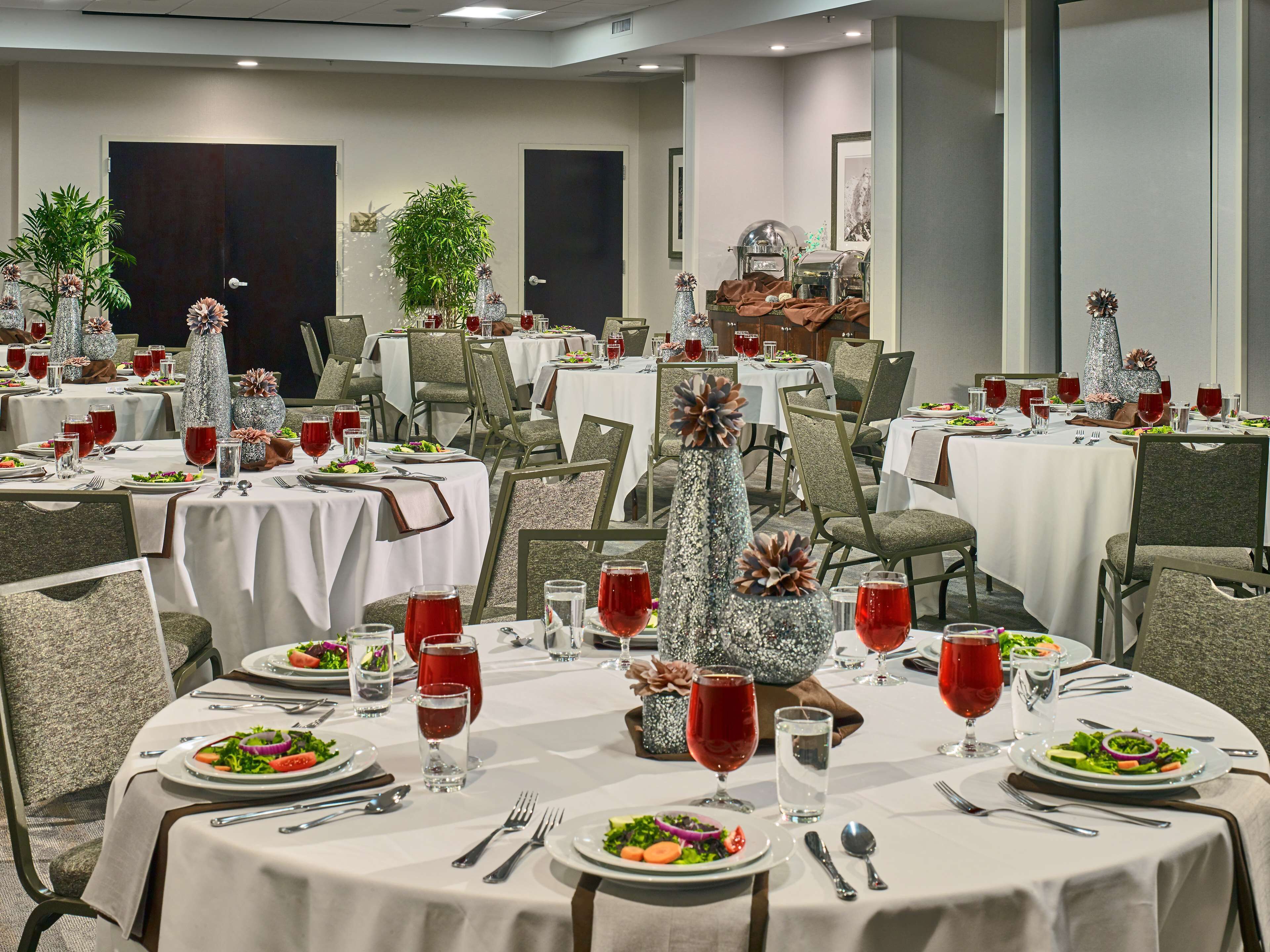 A dining area with round tables, each set with plates, cutlery, and red beverages.