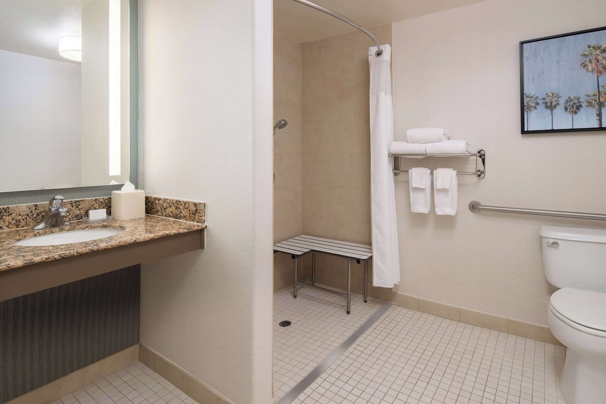 Un baño con lavamanos de encimera de granito, ducha con puerta de cristal y retrete.
