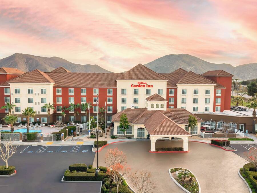 Un Hilton Garden Inn con piscina, varios pisos y un paisaje montañoso al fondo.
