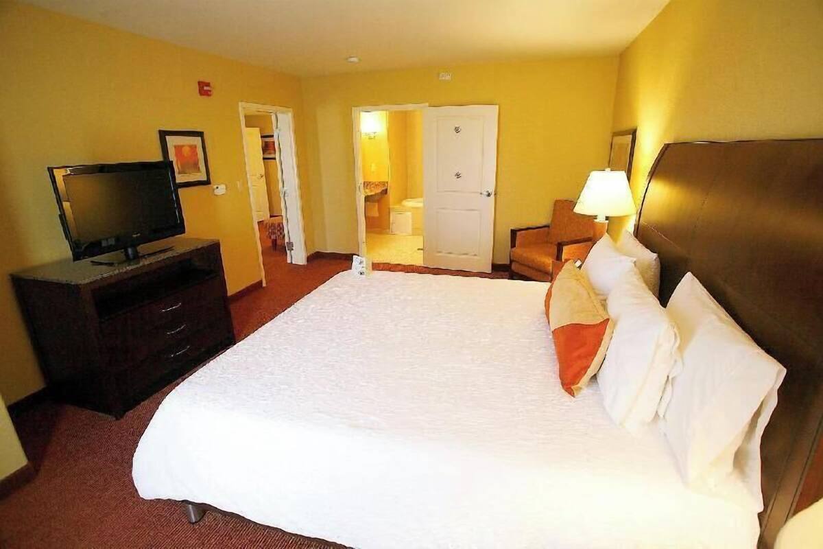 Una habitación de hotel con una cama, un televisor en un tocador, una lámpara y una puerta que da a un baño.