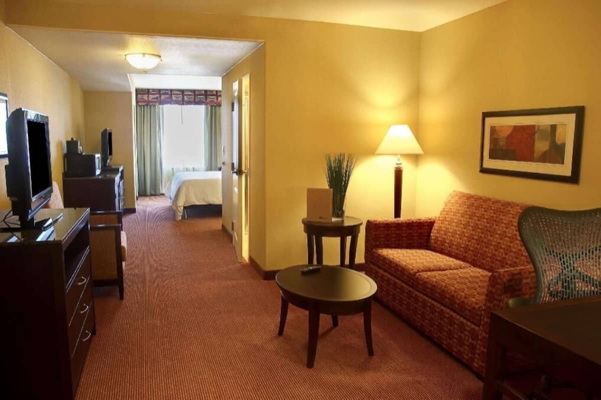 Una habitación de hotel con sofá, una mesita, televisor, lámpara y cama.