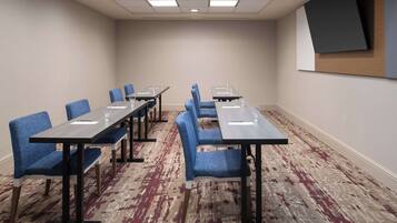 A conference room with a long table, blue upholstered chairs, and a carpeted floor.