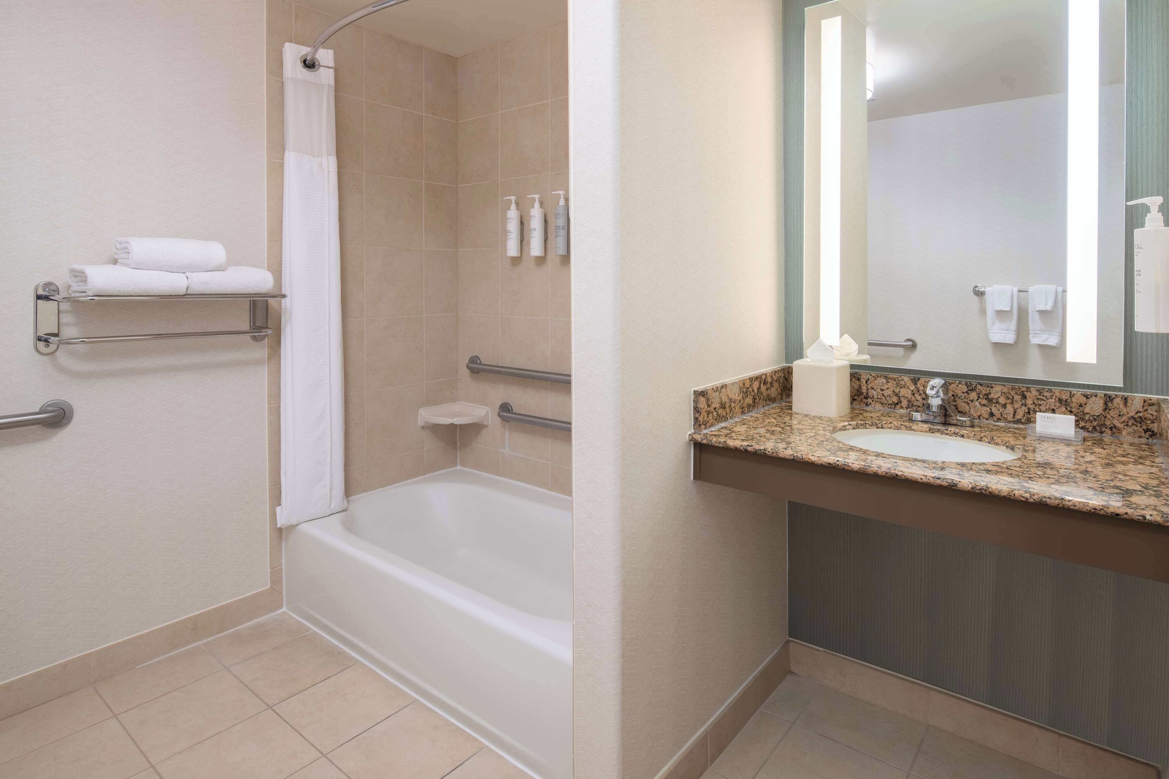 Ein Badezimmer mit Badewanne, Dusche, Waschbecken mit Granitablage und Spiegel.