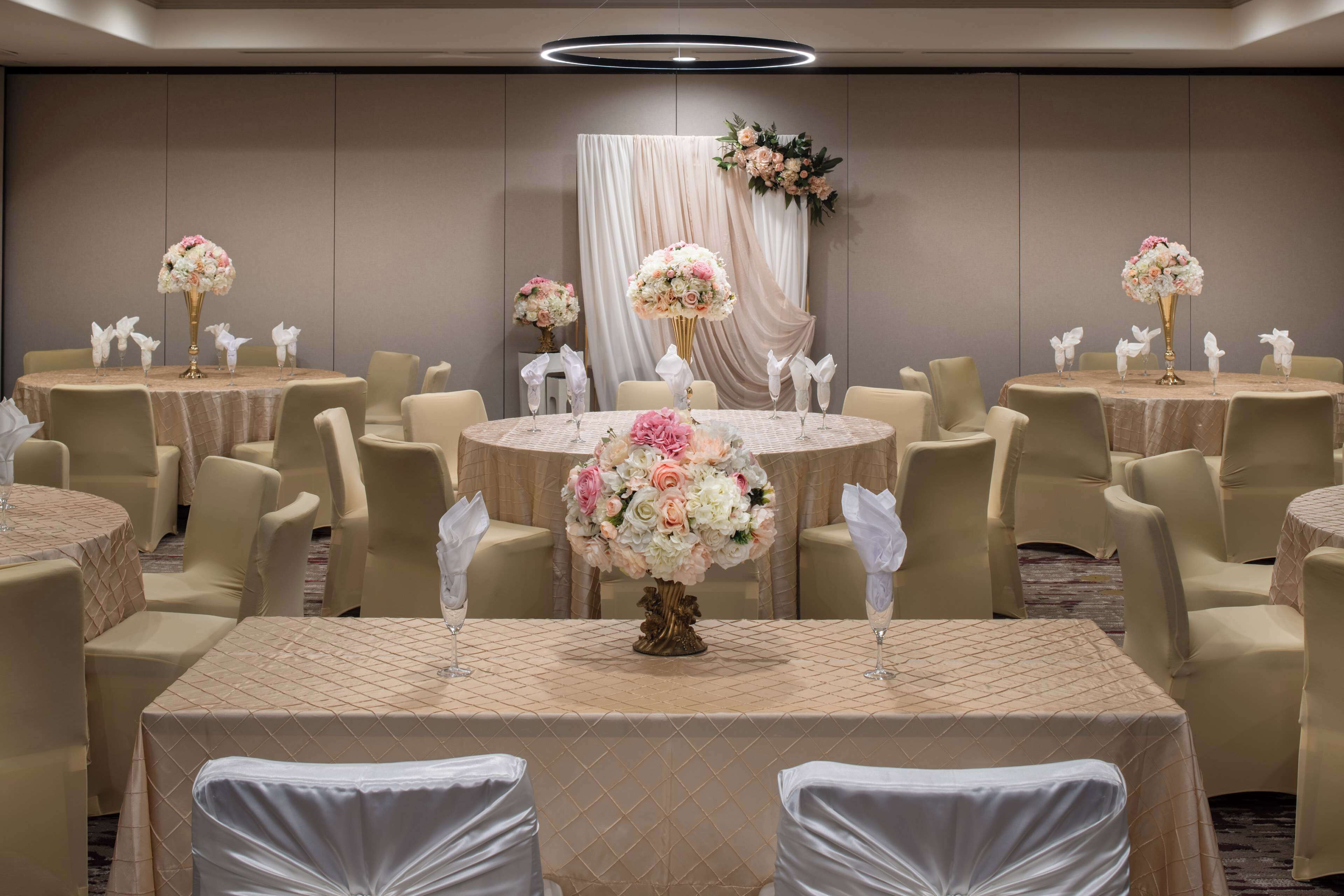 A banquet hall with round tables, each with a floral centerpiece and white napkins.