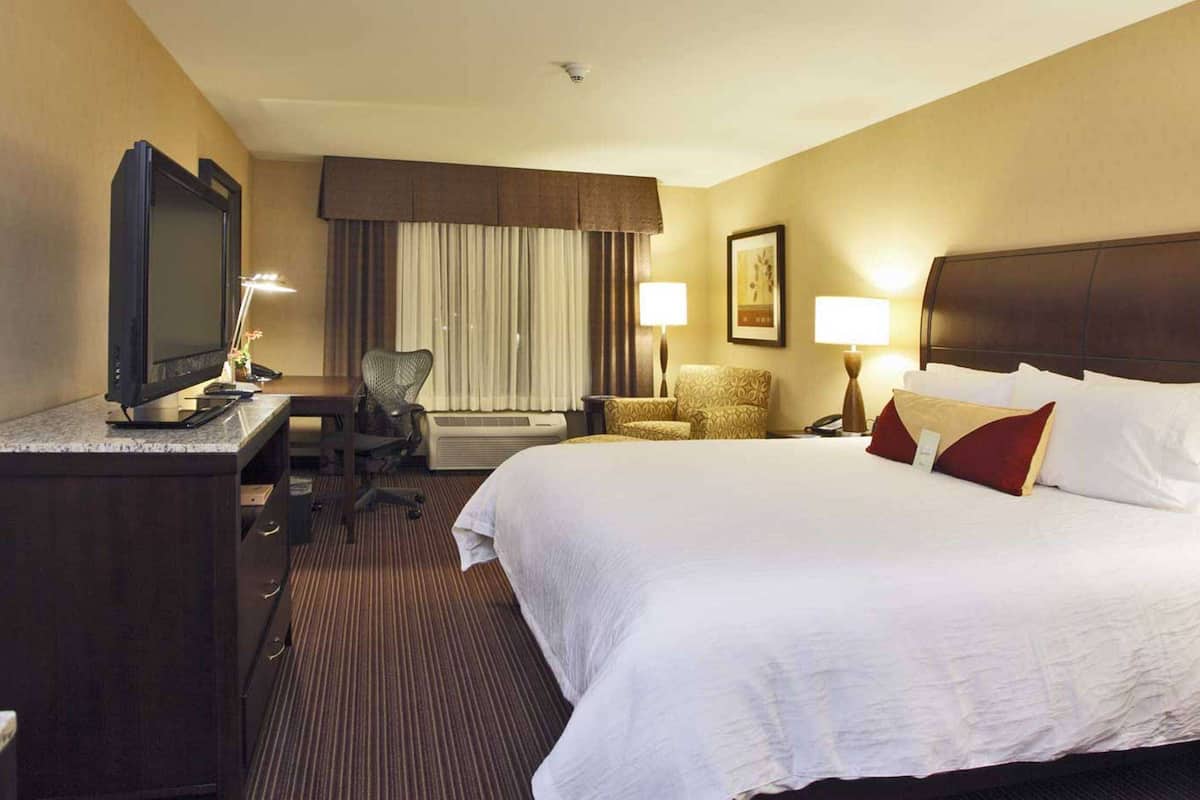Una habitación de hotel con una cama grande, un escritorio con televisor, una silla y dos lámparas de noche.