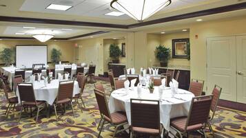 A conference room with round tables set for meetings, equipped with chairs and white tablecloths.