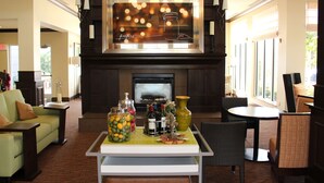 A cozy living area with a fireplace, comfortable seating, and a table with various items. - Hilton Garden Inn Clovis (Clovis)