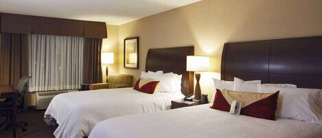 A hotel room with two beds, a desk, a chair, and a window with curtains.
