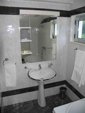 Un baño con lavamanos pedestal, espejo, ventana y zona de ducha.