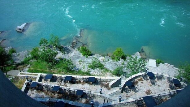 Une vue sur la rivière, avec une eau turquoise et limpide, un paysage rocheux et des espaces de détente en plein air, comprenant des chaises et des tables.