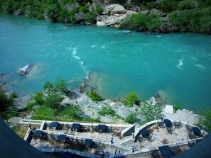 Une vue sur la rivière, avec une eau turquoise et limpide, un paysage rocheux et des espaces de détente en plein air, comprenant des chaises et des tables.