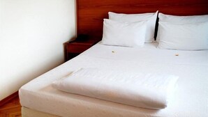 Un lit bien fait, avec du linge de lit blanc, une tête de lit en bois et un plancher en bois.