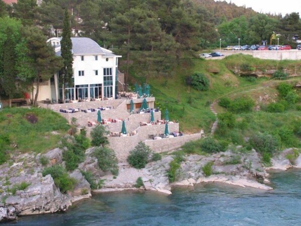 Un hôtel doté d’une terrasse extérieure donnant sur un plan d’eau, entouré de verdure et de collines.