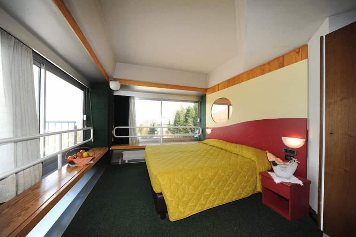 Ein Hotelzimmer mit einem Bett, einem Nachttisch, einem Fenster mit Blick, einer Bank und einem kleinen Tisch mit einem Korb.