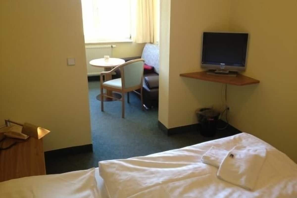 Una habitación de hotel con una cama, un escritorio con computadora, una silla y una ventana con cortinas.