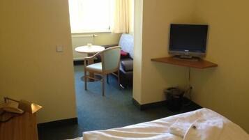 Ein Hotelzimmer mit Bett, Schreibtisch inklusive Computer, Stuhl und einem Fenster mit Vorhängen.