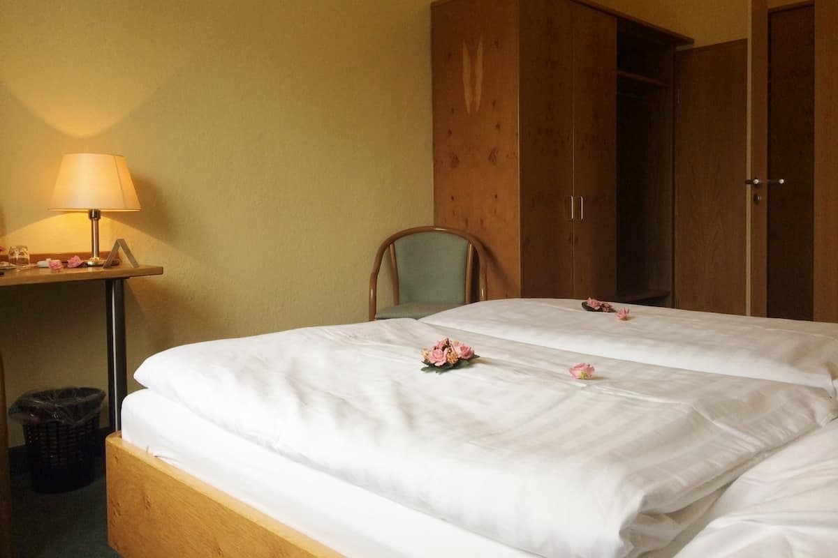 Habitación de hotel con dos camas, un armario de madera, una silla, un escritorio con lámpara y un cesto de basura.