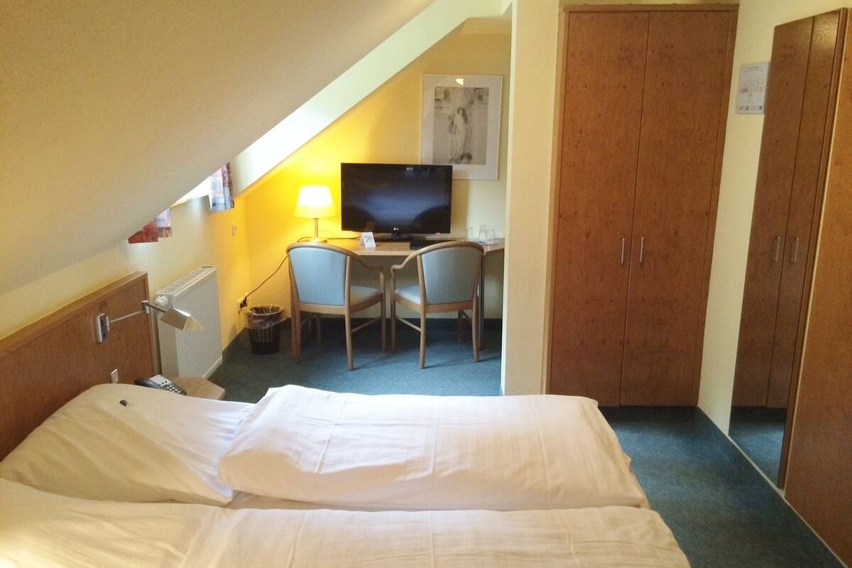 Habitación de hotel con cama, escritorio con silla, televisión y armario.