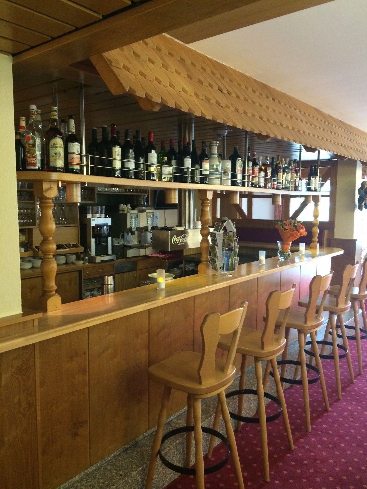 Eine Bar mit hölzernen Barhocker, Regalen voller Flaschen, einem Coca-Cola-Kühlschrank und einer Holzzielung.