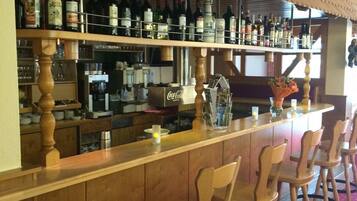 A bar area with wooden bar stools, shelves stocked with various bottles, a Coca-Cola refrigerator, and a wooden ceiling.