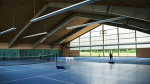 Una cancha de tenis interior con techos altos y ventanas amplias.