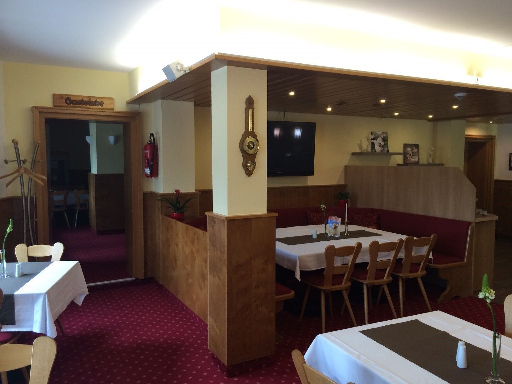 A restaurant with wooden booths, white tables, and a red carpeted floor.