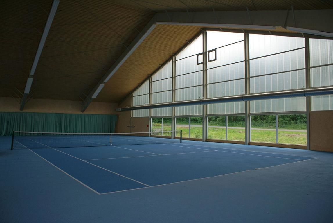 An indoor tennis court with a high ceiling and large windows.