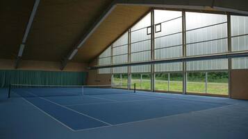 An indoor tennis court with a high ceiling and large windows.