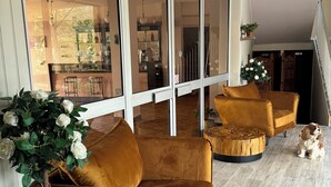 A spacious living area with a large sliding glass door leading to a kitchen and dining area. There are two mustard-colored sofas and a wooden coffee table. A potted plant with white flowers is placed near the sofas. - Hôtel Céline (Coti-Chiavari)