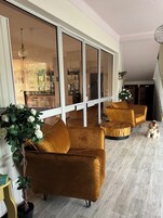 Amplia sala de estar con un gran ventanal corredero que da a una cocina y comedor. Hay dos sofás de color mostaza y una mesa de centro de madera. Una planta en maceta con flores blancas se encuentra cerca de los sofás.
