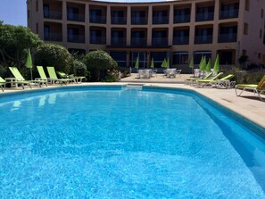 A swimming pool with lounge chairs and umbrellas, surrounded by a building with multiple balconies. - Hôtel Céline (Coti-Chiavari)