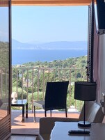 Un balcón con vistas al mar y a las colinas, una mesa, dos sillas y una lámpara.