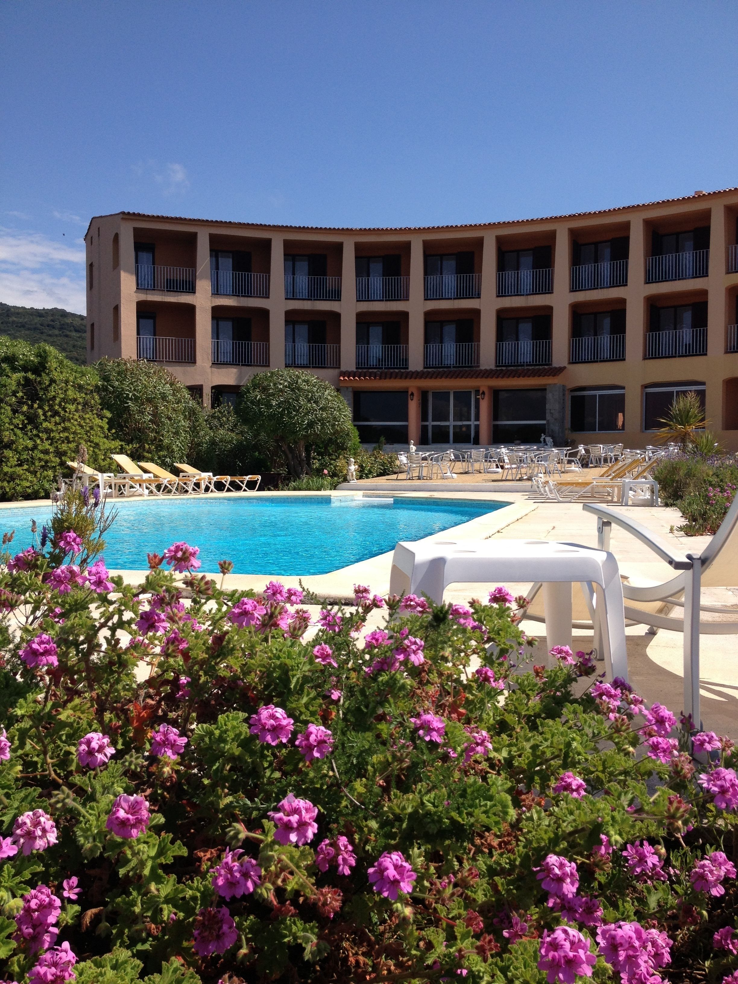 Ein Hotel mit Swimmingpool, Außenbereich zum Sitzen und einem Gebäude mit mehreren Balkonen.