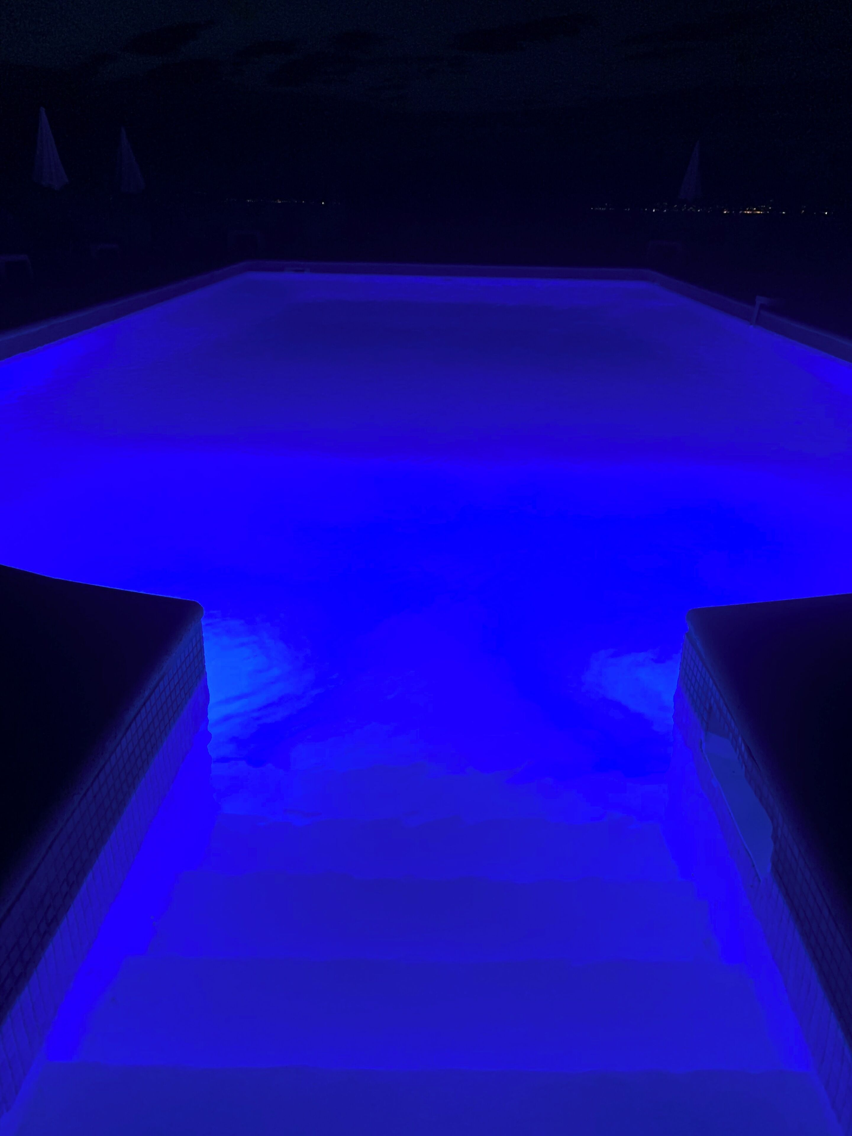 A swimming pool with a blue-lit interior, surrounded by a dark poolside area.