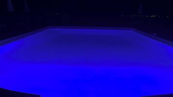 A swimming pool with a blue-lit interior, surrounded by a dark poolside area.