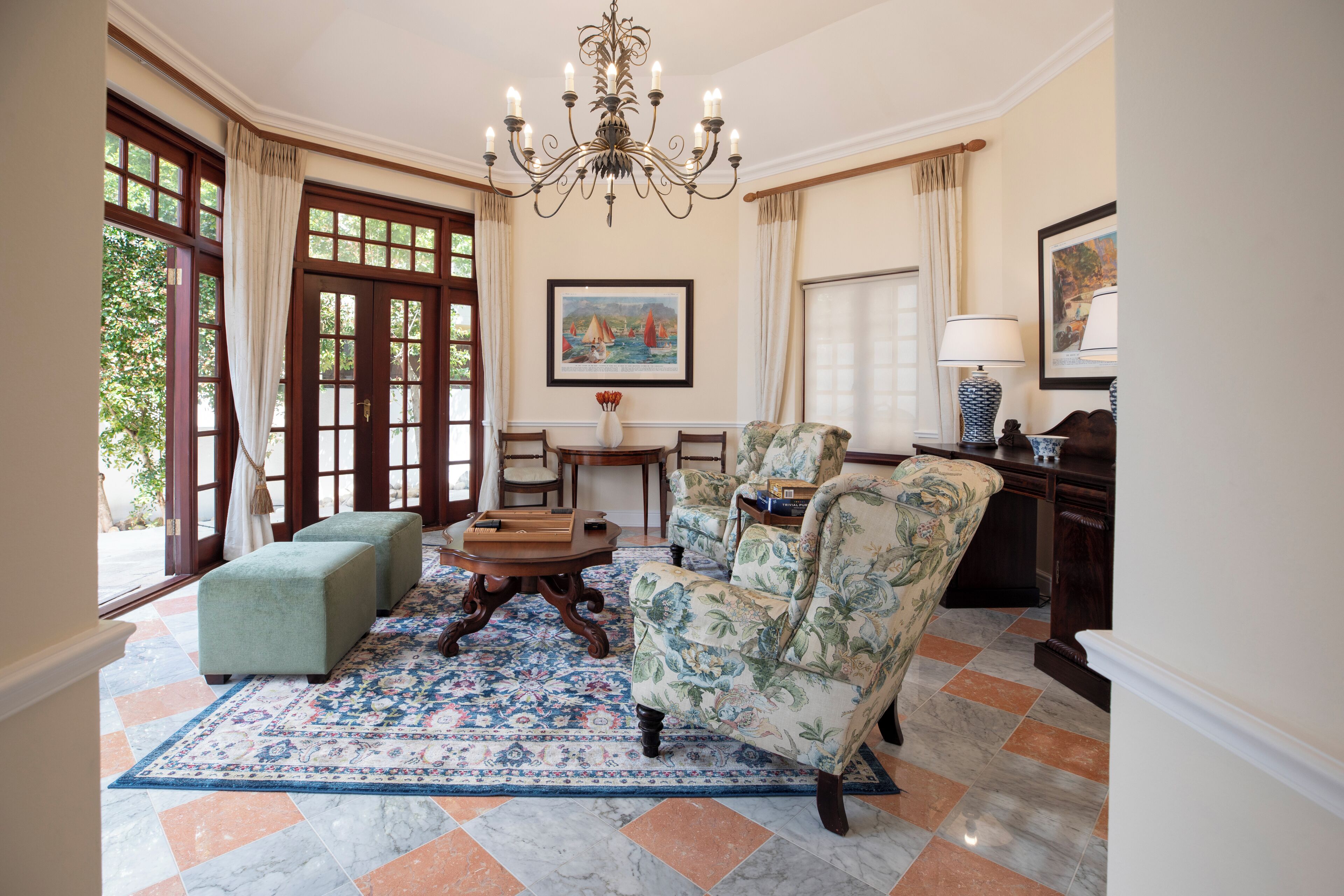 Uma sala de estar ampla com um lustre grande, duas poltronas, um sofá, uma mesa de centro e um tapete estampado.