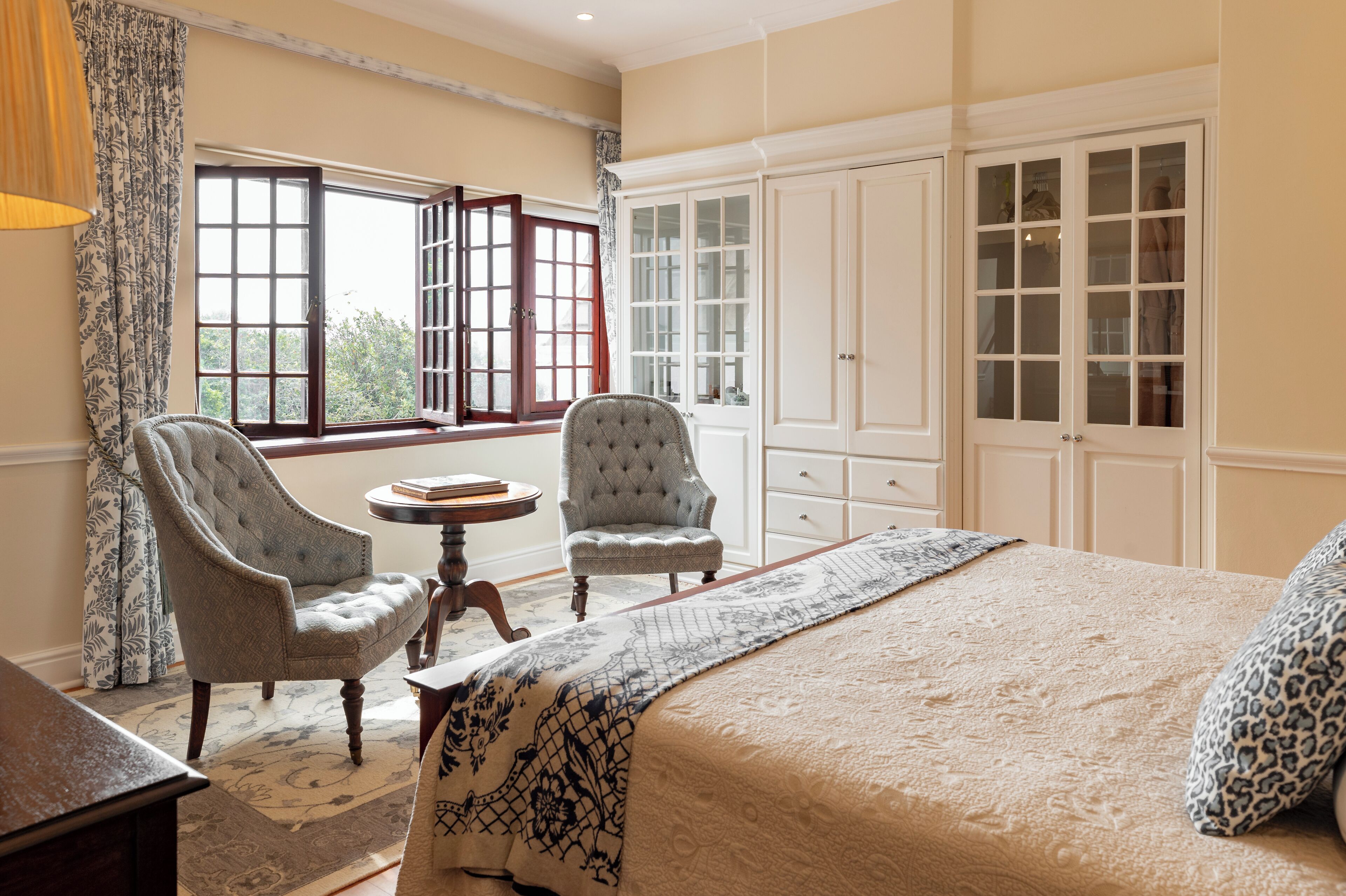 Um quarto com uma cama grande, duas poltronas, uma mesinha redonda e um guarda-roupa.