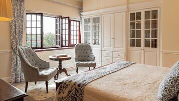 Um quarto com uma cama grande, duas poltronas, uma mesinha redonda e um guarda-roupa.