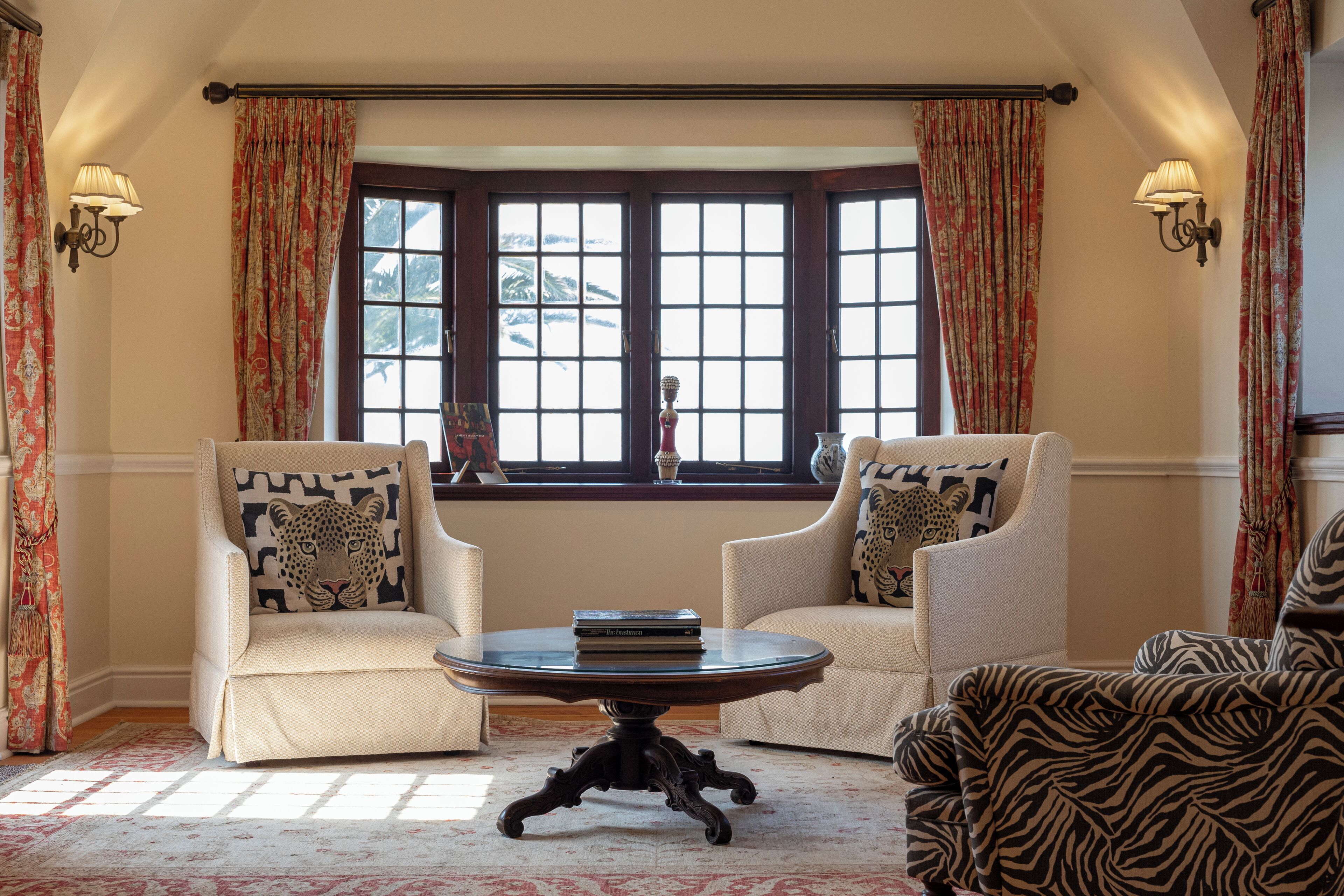 Une pièce avec deux fauteuils, une table ronde et une fenêtre avec des rideaux.