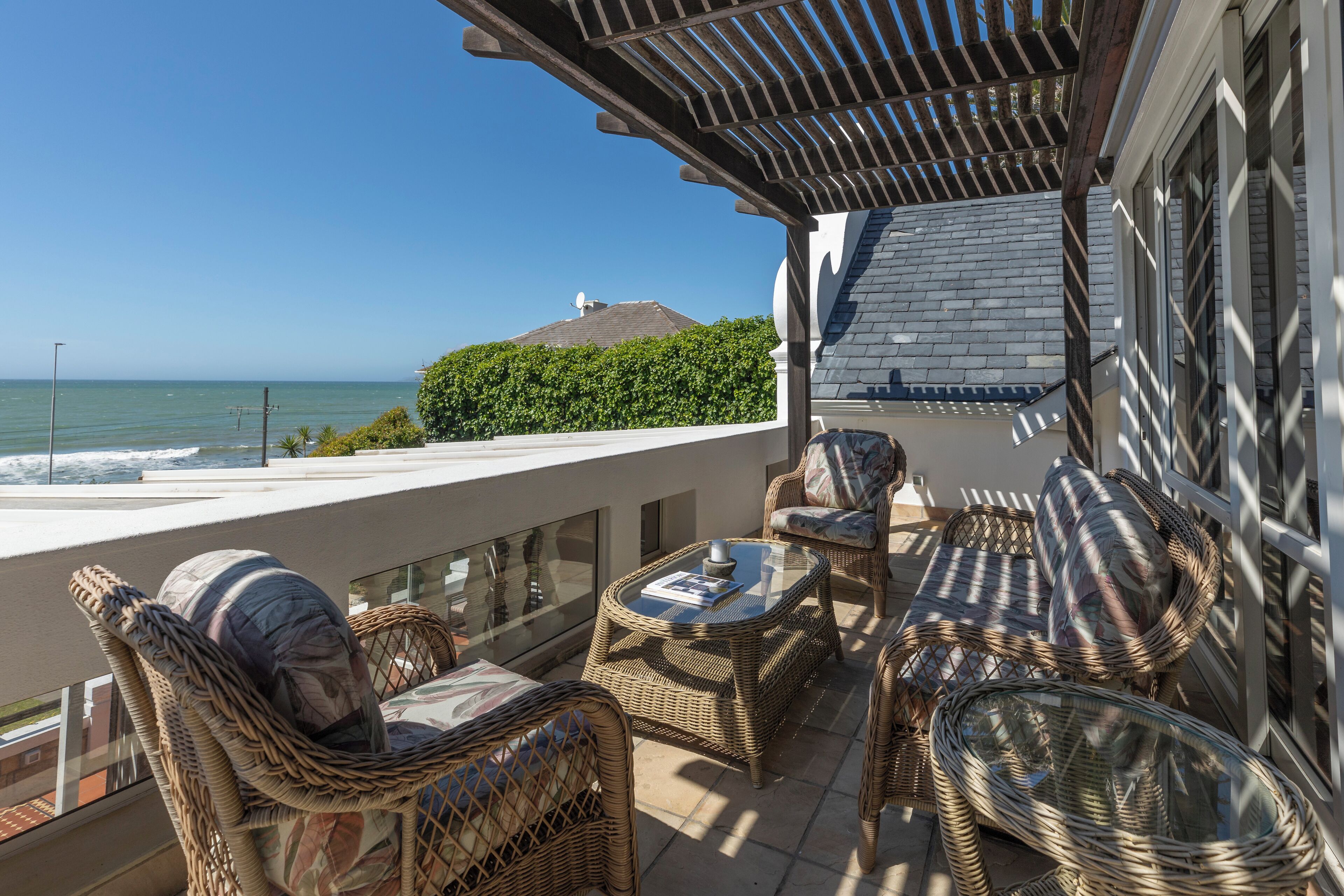 A balcony with wicker furniture, a glass table, and a view of the ocean.