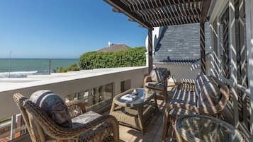 A balcony with wicker furniture, a glass table, and a view of the ocean.