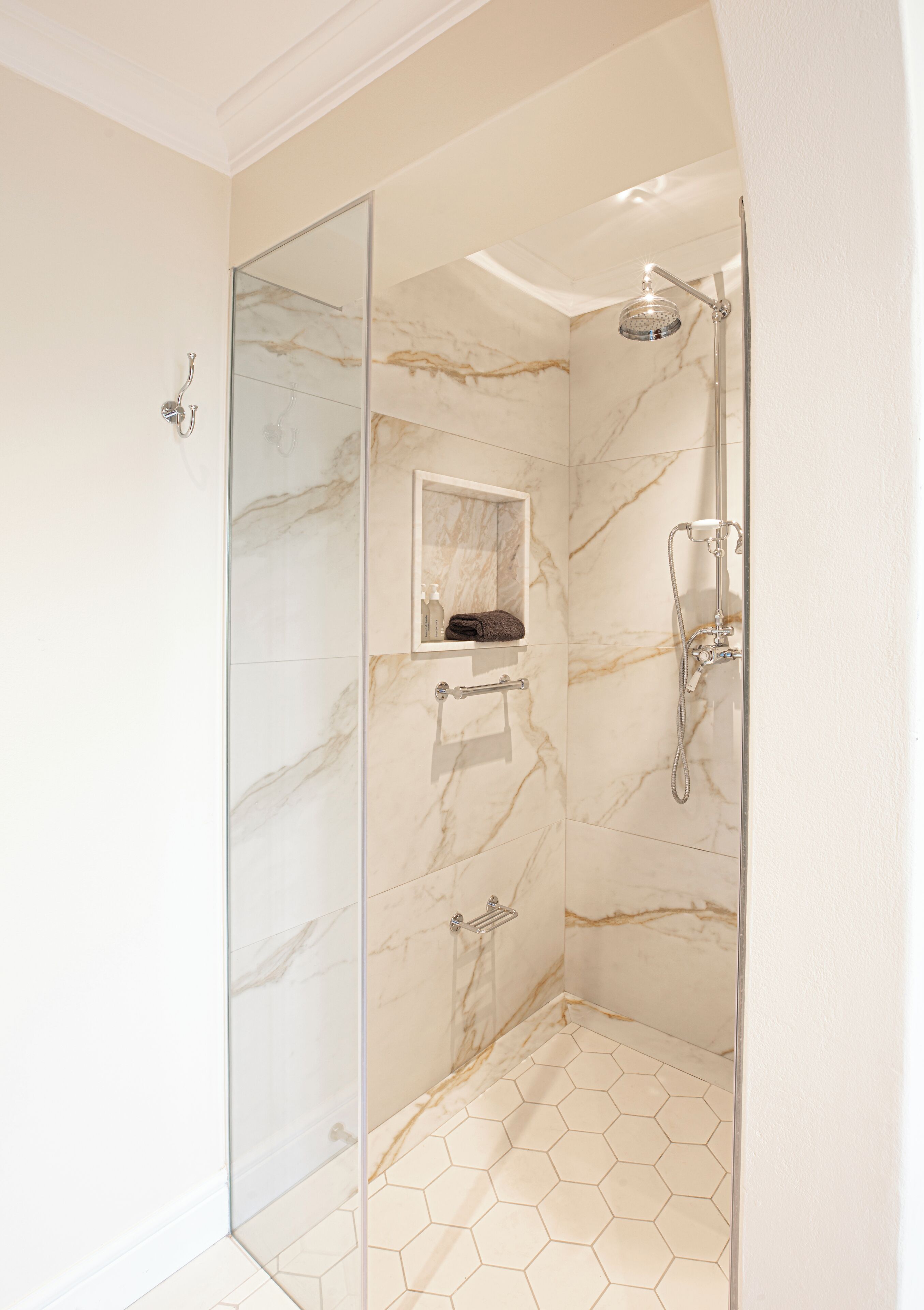 A modern shower with a glass door, marble walls, and a hexagonal tile floor.